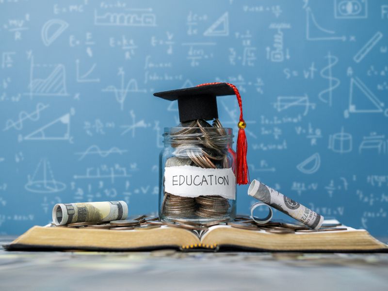 prikaz knjige na kojoj je novac, diplomske kape i table u pozadini sa matematičkim sibolima