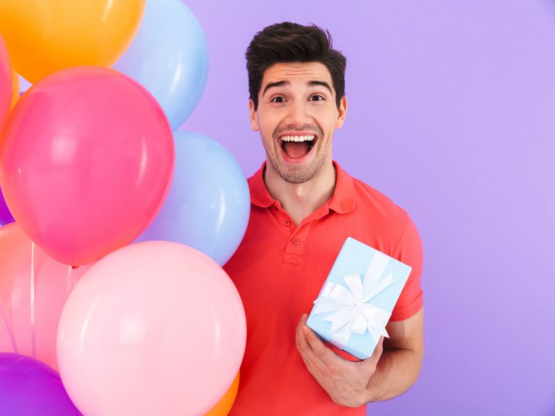 momak drži poklon u ruci i baloni pored njega