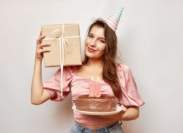 devojka drži rođendansku tortu u ruci na kojoj su svećice sa brojem 18 i poklon u ruci